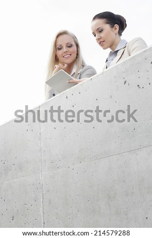 Low angle view of young female business executives using digital tablet while standing on terrace against sky
