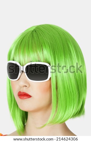 Young woman wearing green wig over gray background