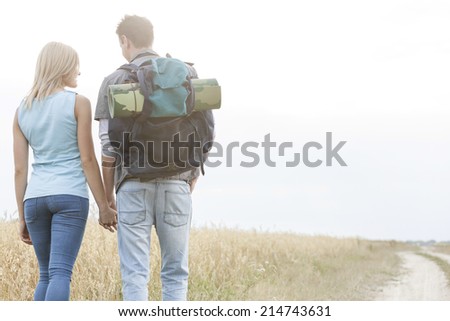 Rear view of young hiking couple holding hands while walking in countryside