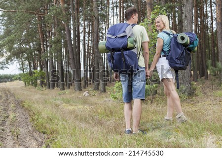 Full length rear view of young hiking couple holding hands in countryside