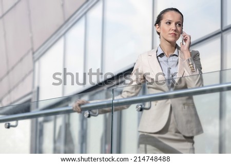 Confident young businesswoman using cell phone at office balcony
