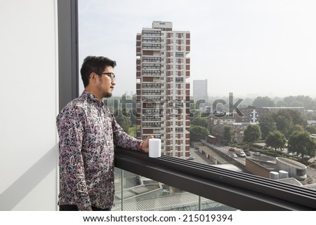 Young man with coffee mug looking out through window at home