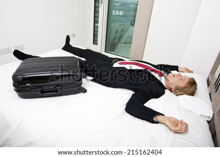Mid adult businessman with luggage sleeping in bed at home