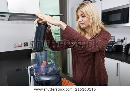 Young blond woman juicing carrots in kitchen