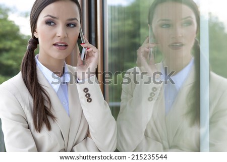 Beautiful businesswoman answering cell phone by glass door