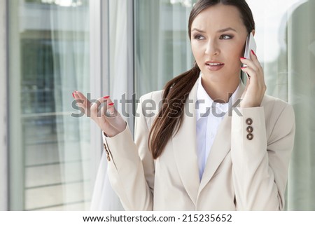 Businesswoman gesturing while answering cell phone against glass door