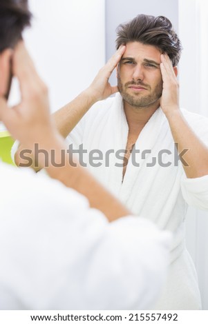 Reflection of man in bathrobe suffering from headache