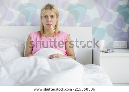 Portrait of young woman taking temperature with thermometer