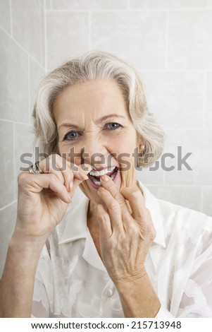 Portrait of senior woman flossing teeth in bathroom