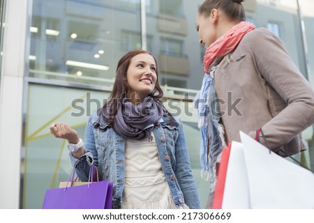Low angle view of female friends with shopping bags looking at each other against store