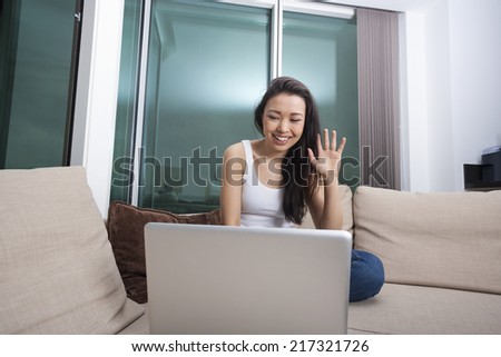 Smiling young woman waving in front of laptop on sofa