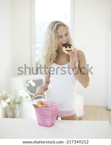 Portrait of happy woman eating cookie while winking at kitchen counter