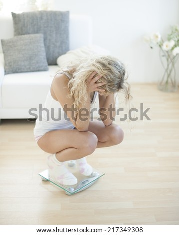Disappointed young woman crouching on weighing scale