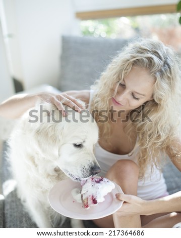Beautiful woman feeding cake to dog in house