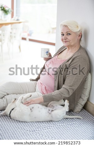 Portrait of happy senior woman having coffee while stroking dog at home