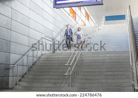 Full length of businessman and businesswoman walk down stairs at railway station