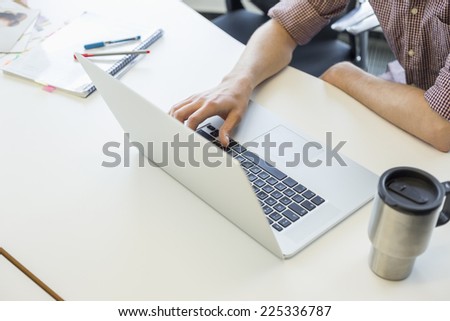 Cropped image of man using laptop at desk in creative office