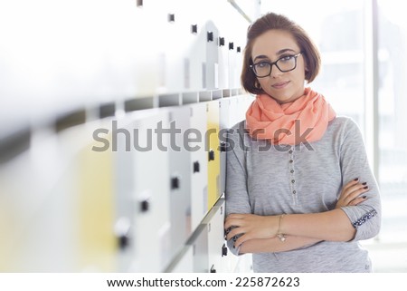 Portrait of confident businesswoman standing arms crossed in locker room at creative office