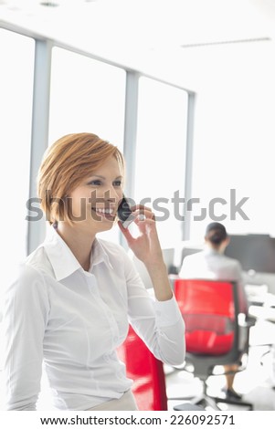 Young businesswoman talking on cell phone with colleagues in background at office