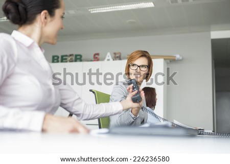 Young businesswoman handing telephone to colleague in office