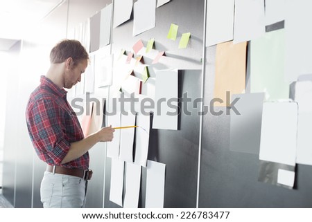 Businessman analyzing documents on wall at creative office