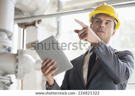 Young male engineer with digital tablet pointing away in industry