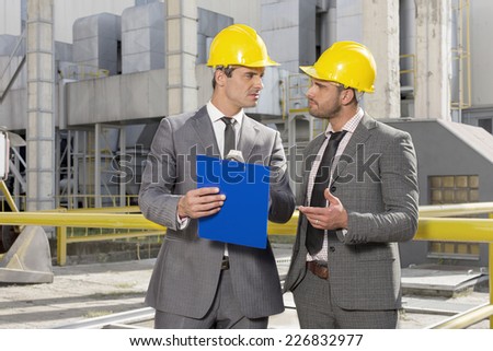 Young male engineers with clipboard discussing at construction site