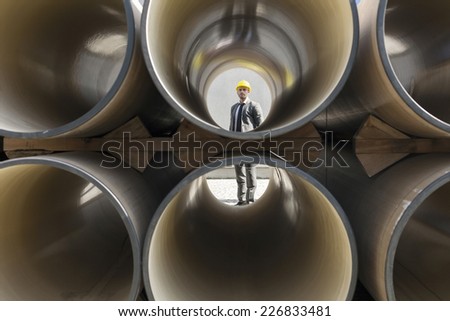 Full length of young male architect through stacked pipes at construction site