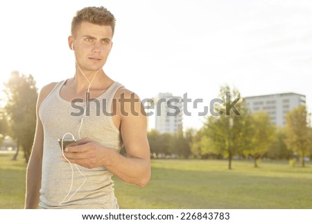 Young jogger looking away while listening music through cell phone in park