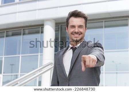 Portrait of smiling businessman pointing at you outside office building