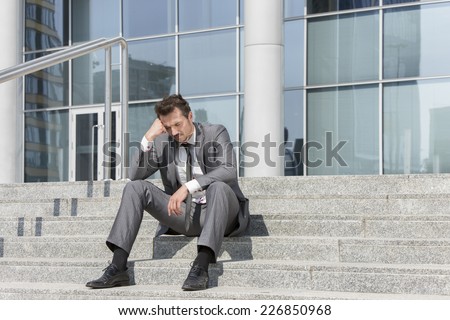 Full length of stressed businessman sitting on steps outside office