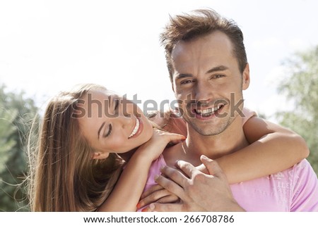 Smiling young woman embracing man from behind in park