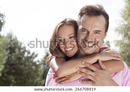 Portrait of happy young man being embrace by woman from behind in park
