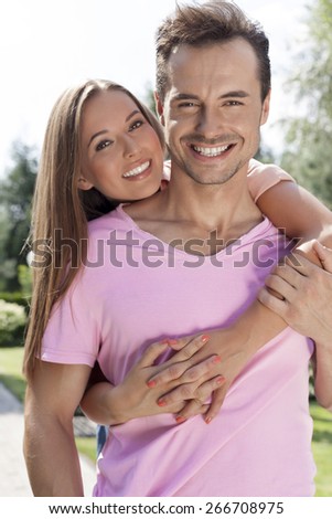 Portrait of beautiful young woman embracing man from behind in park