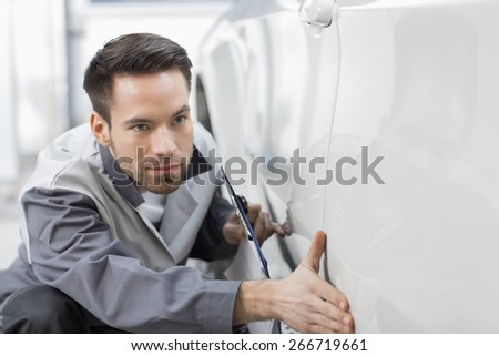 Young automobile mechanic examining car in repair store