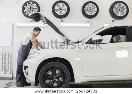 Full length side view of male mechanic examining car engine in repair shop