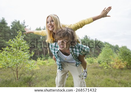 Happy woman enjoying piggyback ride on man in forest