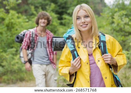 Smiling female backpacker looking away with man standing in background at forest