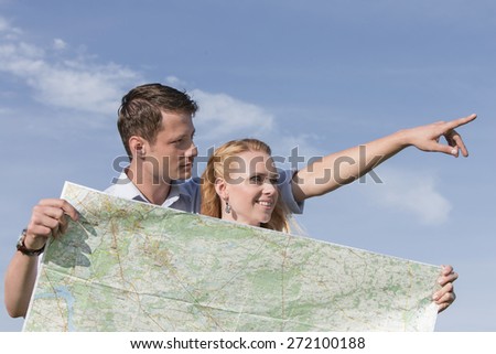 Woman holding map while man pointing away against sky