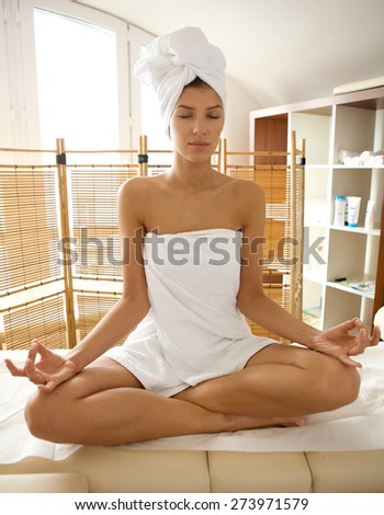 Young woman wrapped in towel doing yoga, eyes closed