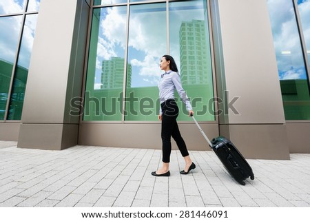 Full length side view of young businesswoman walking with luggage on sidewalk against building