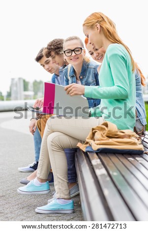 University students studying while sitting on low wall in park