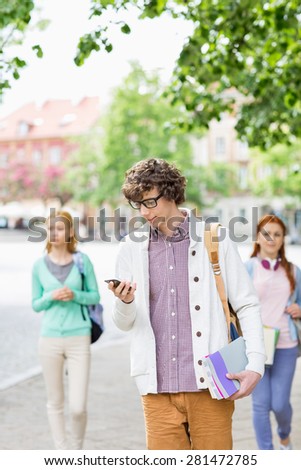 Young male student using cell phone with friends in background on street