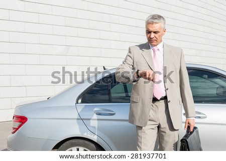 Businessman checking the time in front of car outdoors