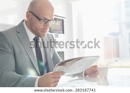 Mid adult businessman having coffee while reading newspaper at home