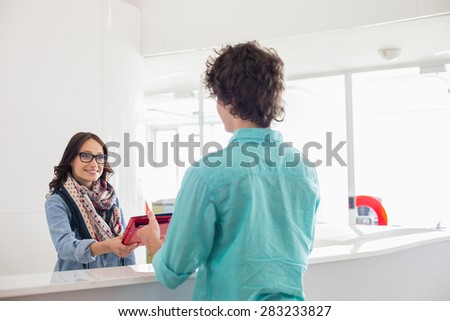 Happy businesswoman giving files to male colleague at counter in creative office