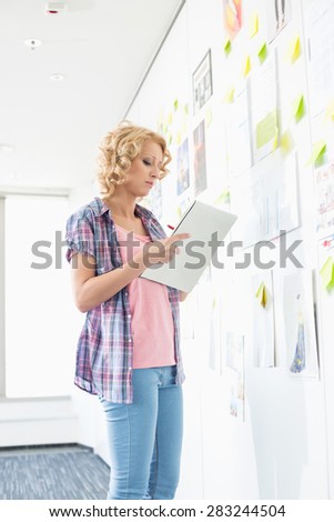Creative businesswoman writing notes by papers stuck on wall in office