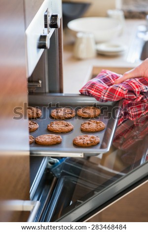 Cropped image of woman\'s hand removing cookie tray from oven in kitchen
