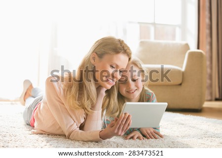 Mother and daughter using digital tablet on floor at home