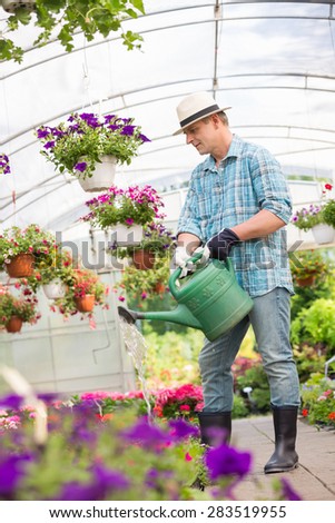 Full-length of man watering flower plants in greenhouse